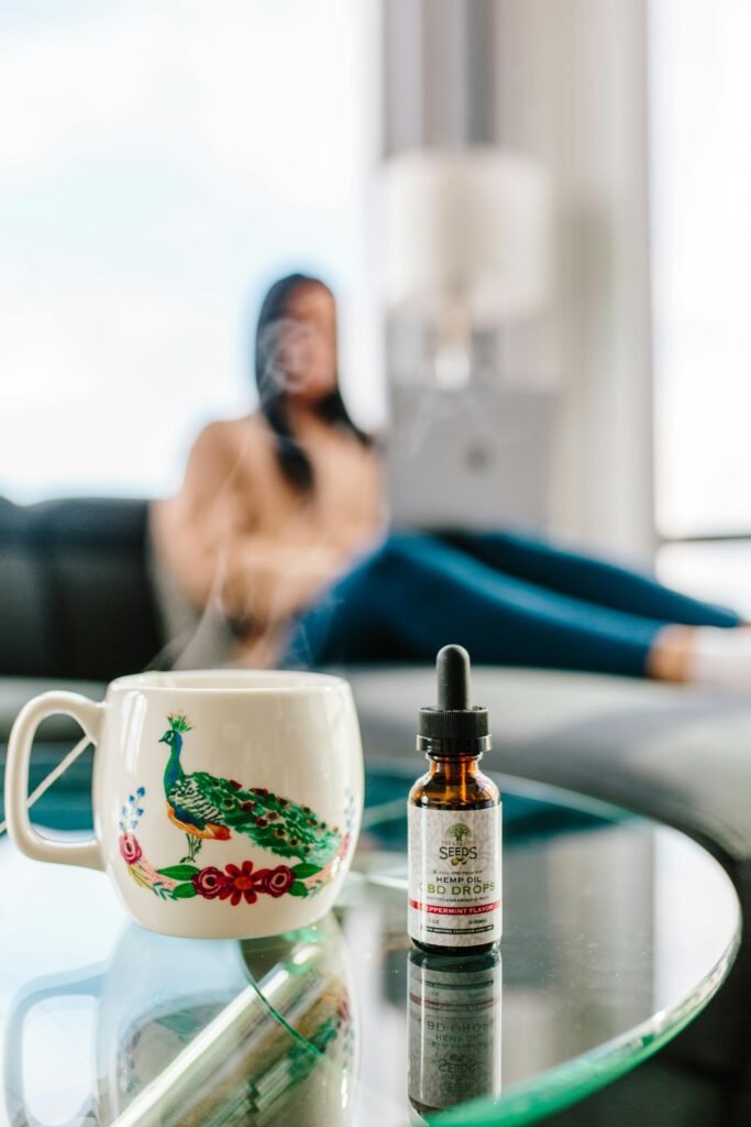 A person enjoys CBD oil and a hot drink on a glass table indoors, creating a cozy setting.