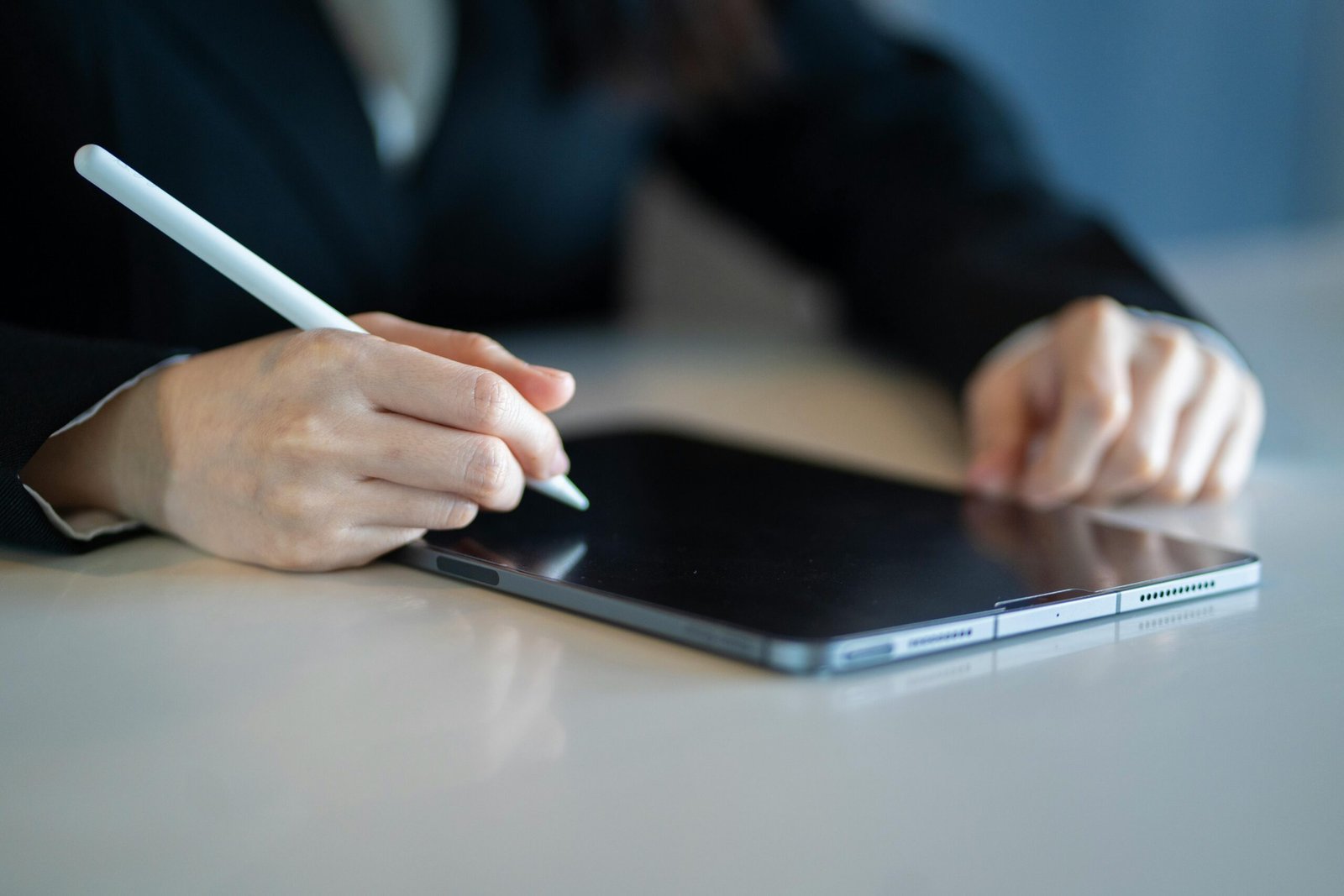 Close-up of a woman using a stylus with a tablet in a modern workspace.